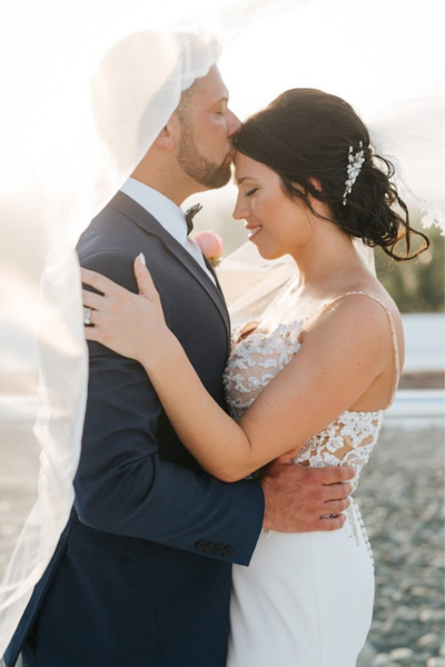 Groom kissing the bride's head with her veil over him at their destination wedding