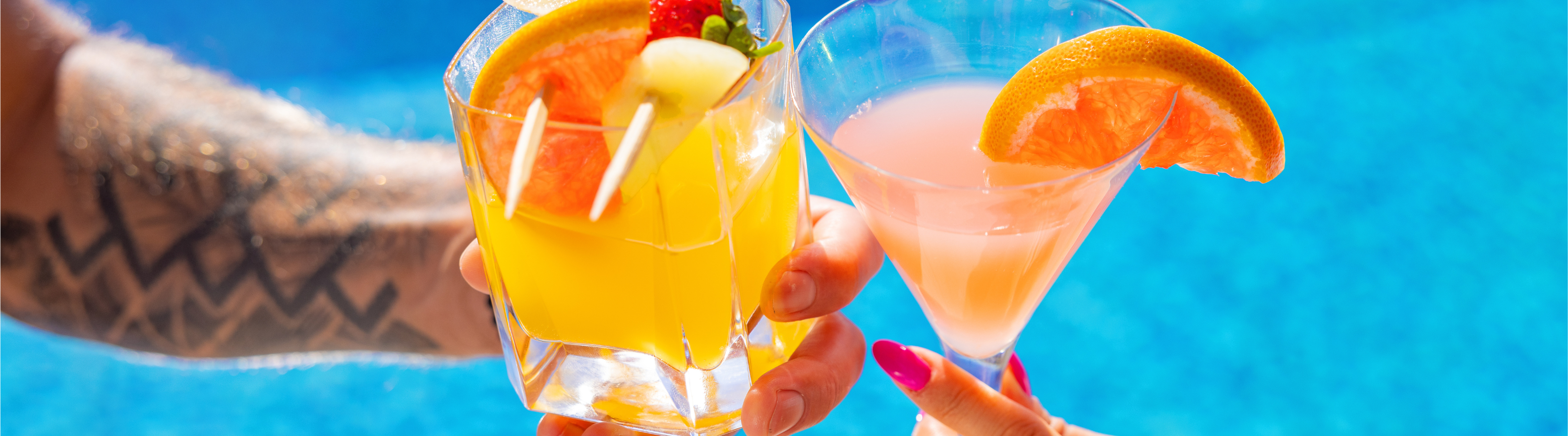 Close up of two cocktails clinking glasses over blue water