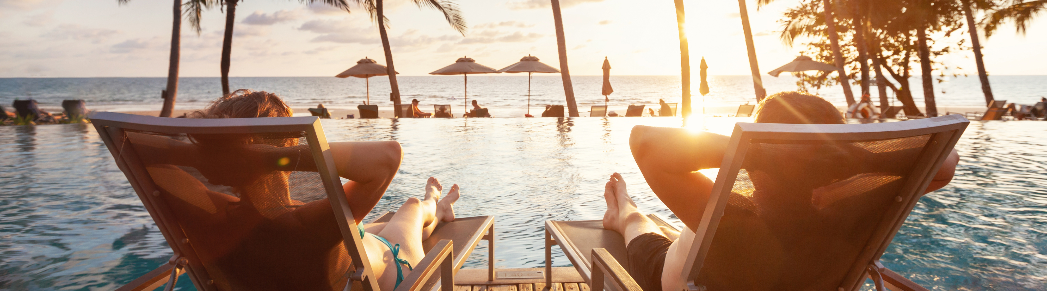 View from behind two people sitting in pool chairs overlooking an infinity pool and the ocean