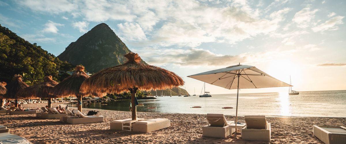 View of the sand and water from the beach at an all-inclusive resort with mountain in the background and umbrellas and beach chairs on the sand 