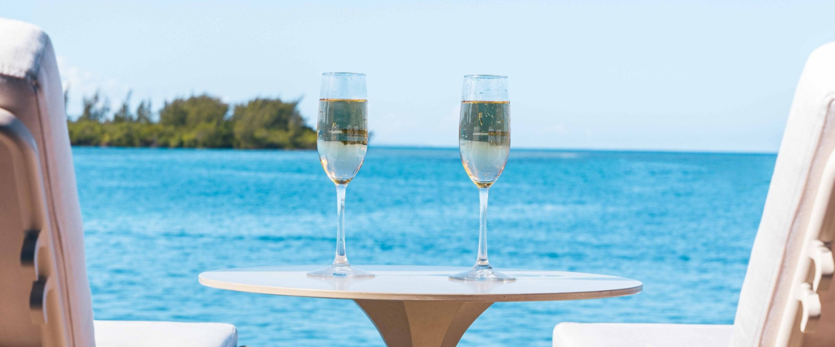 Close up of a table with two champagne glasses overlooking the beach at an all-inclusive resort