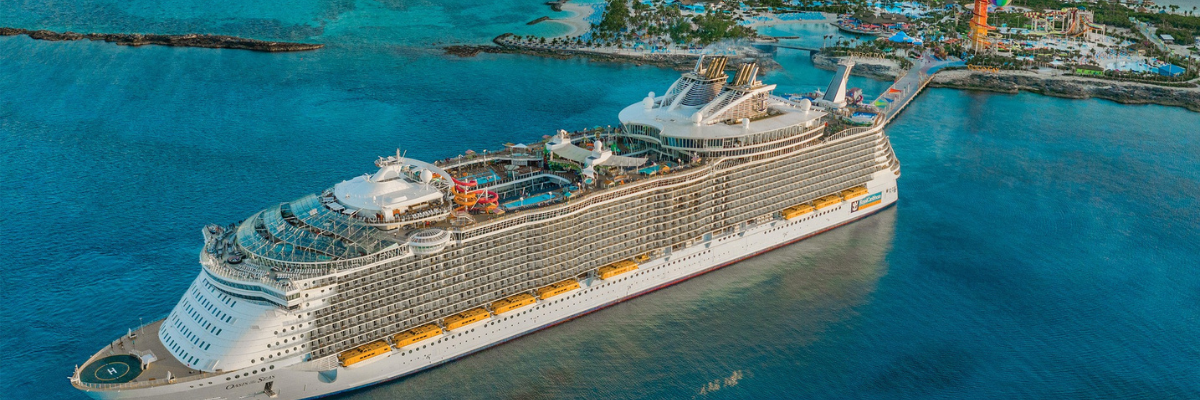 Aerial view of a cruise ship leaving an island with a waterpark in the background