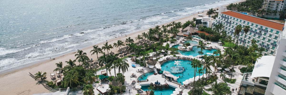 Aerial view of an all inclusive resort in Mexico with views of the resort buildings with pools in the middle of the resort and the sandy beach and ocean 