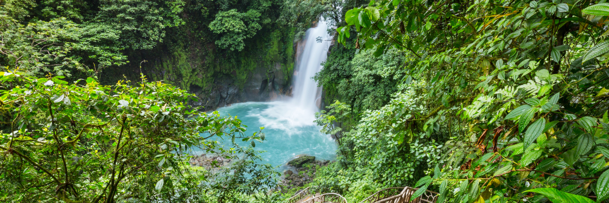 Aerial view of a waterfall in Costa Rica with green foliage all around with a pool of blue water at the base of the waterfall