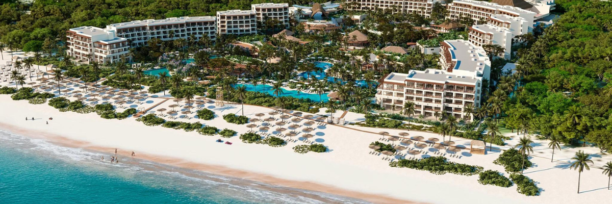 Aerial view of an all inclusive resort in Mexico along the water and surround by green foliage with white sandy beach and pools throughout the resort 