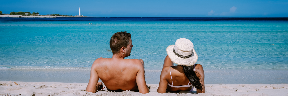 A man and a woman laying down on the beach on propped up on their elbows in the sand