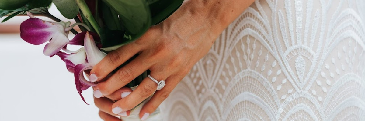 Close up of a brides hand with her engagement ring on her finger holding her bouquet over the dress