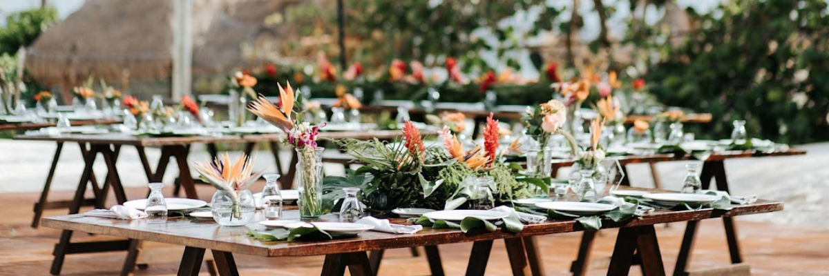 Modern place settings at a destination wedding reception with wooden tables and white place settings and green and floral arrangements