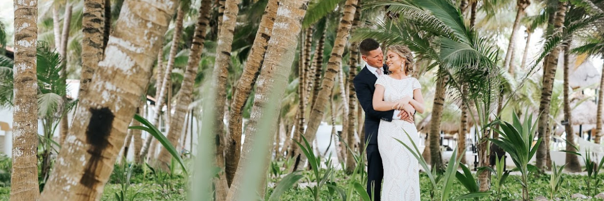 A bride and groom posing at a resort among a lot of palm tree trunks